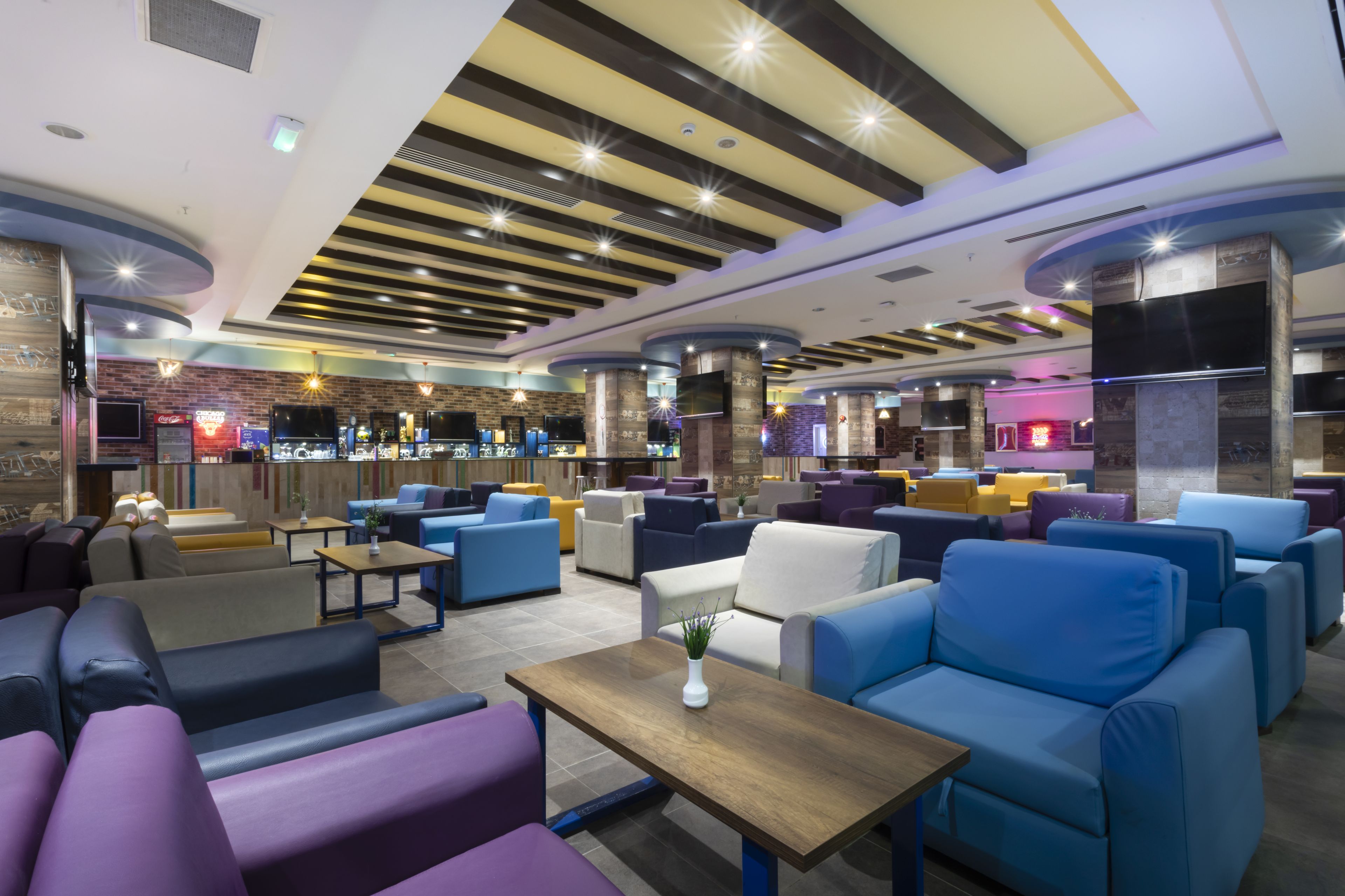 A modern lounge area with sofas and tables, a bar area with a counter, and a television mounted on a pillar.