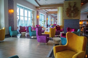 A spacious lobby with multiple seating areas, large windows, and a central decorative column. - Orange County Alanya Family Concept (ANTALYA)