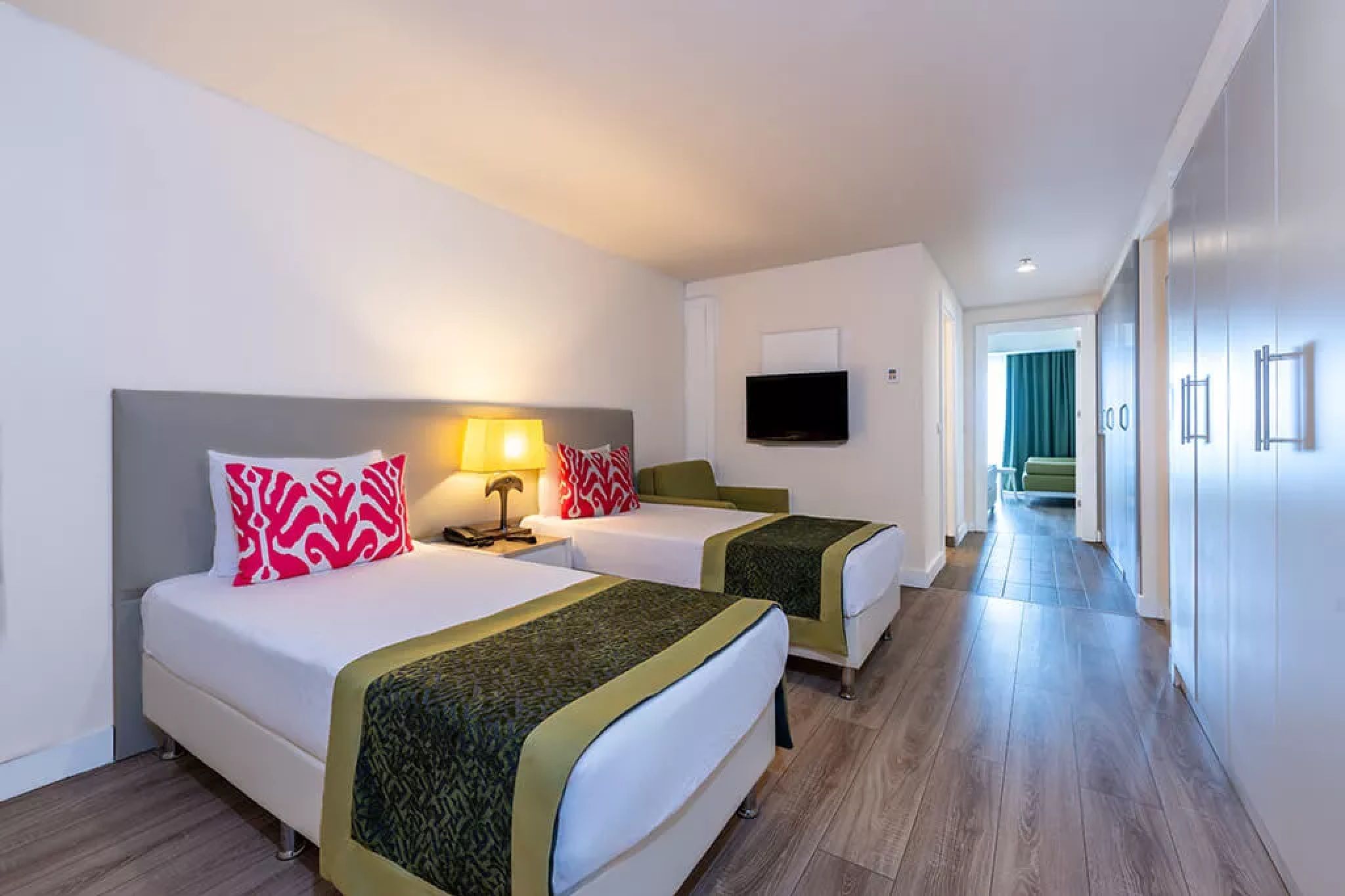 Ein Hotelzimmer mit zwei Betten, einem Fernseher und einem Gang zu einem weiteren Zimmer.