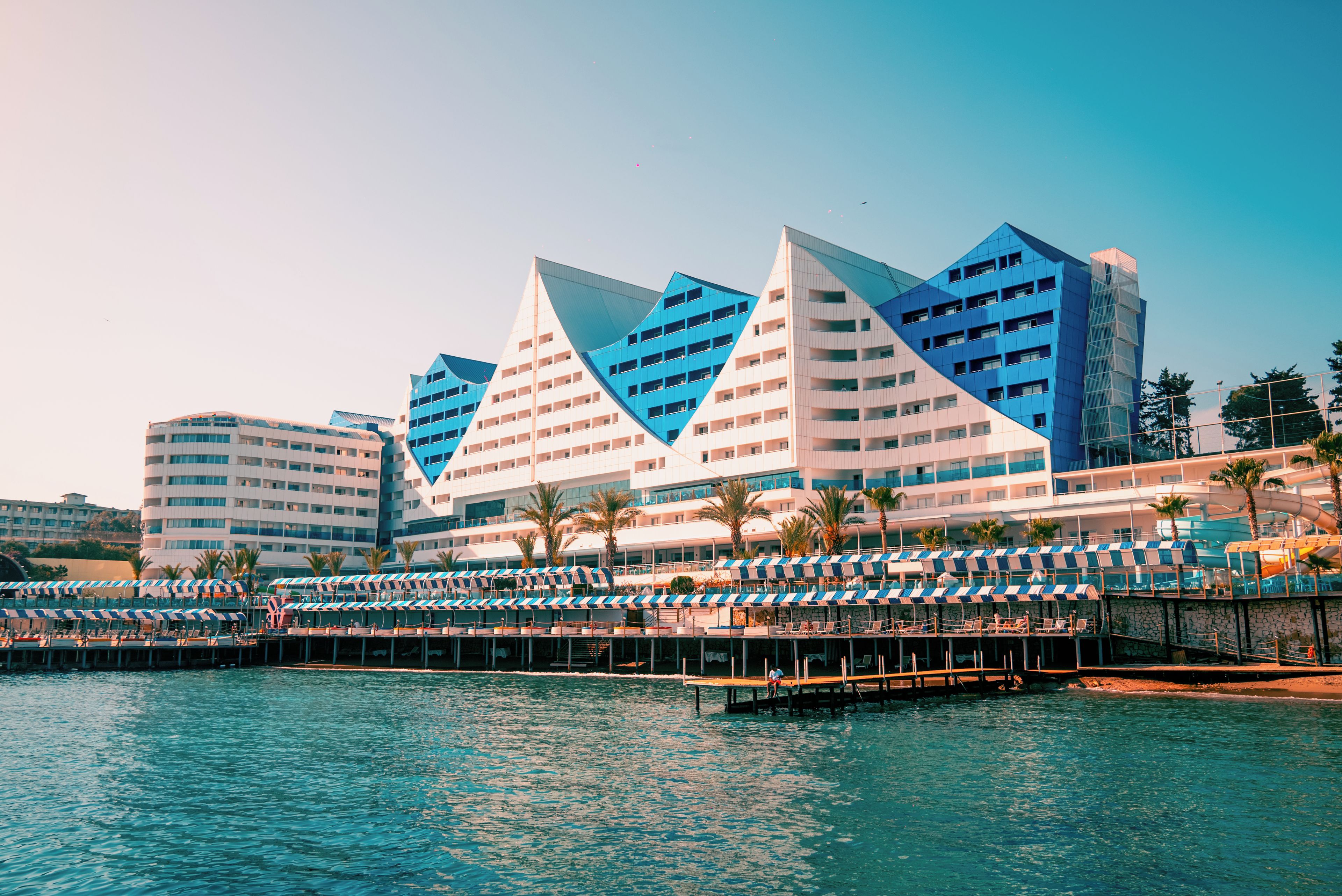 Ein modernes Hotel mit einzigartiger, dreieckiger Architektur, einer Lage am Wasser und einem Poolbereich mit Liegestühlen.