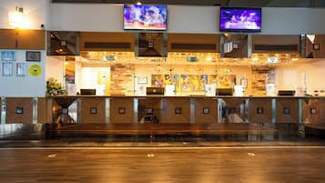 Un'area reception di un hotel con una scrivania in legno, due televisori montati sopra e opere d'arte incorniciate alle pareti.