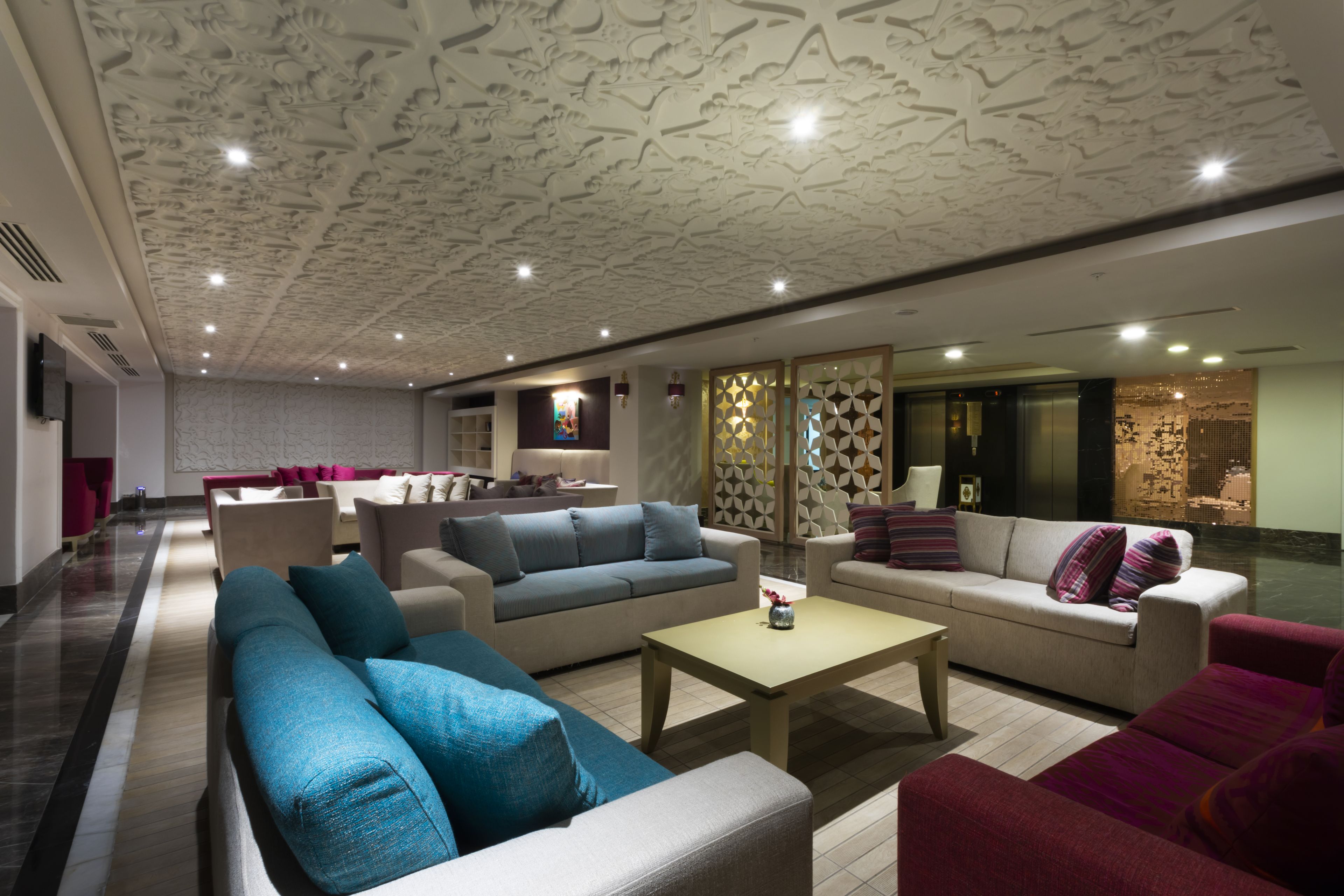 A spacious lobby with sofas, a coffee table, and a patterned ceiling.