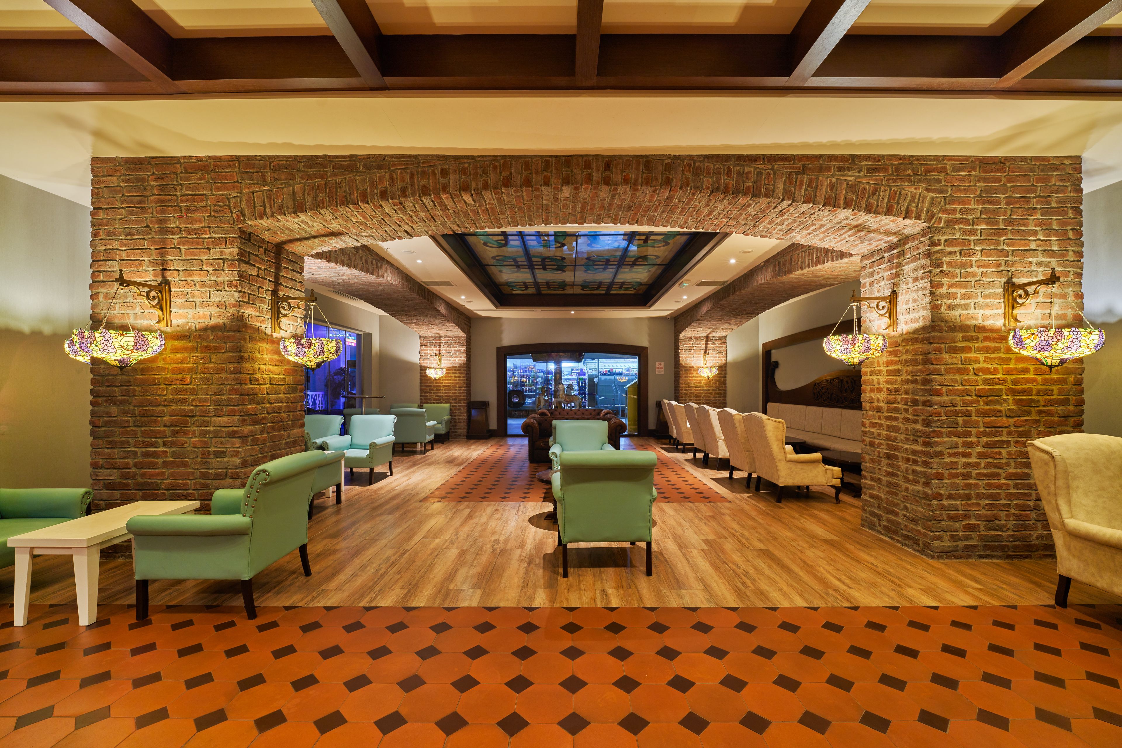 A lobby with brick walls, wooden flooring, and green armchairs.