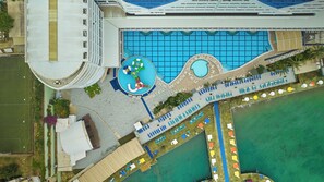 An aerial view of a hotel with a large swimming pool, multiple lounge areas, and a tennis court. - Orange County Alanya Family Concept (ANTALYA)