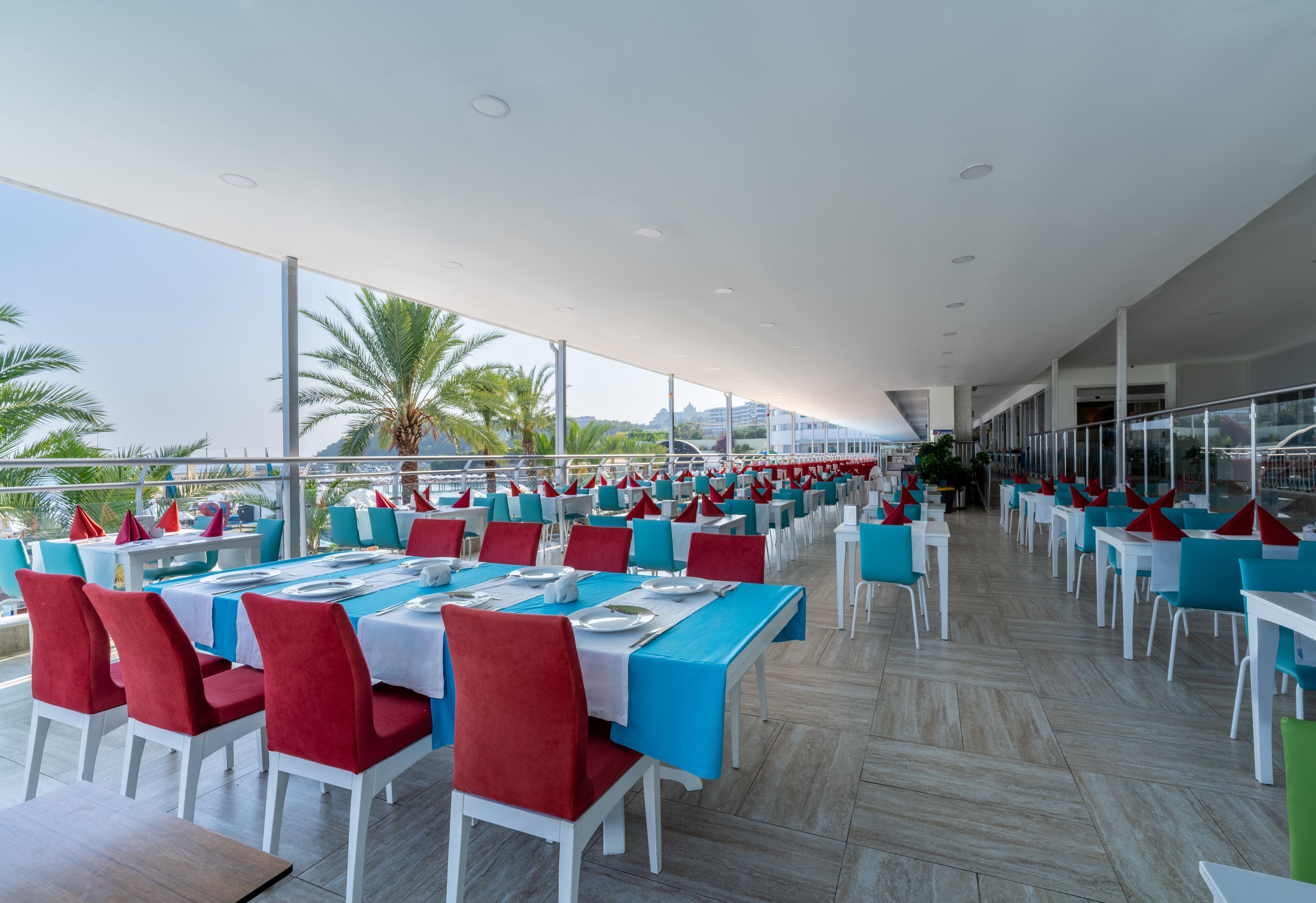Un'ampia zona pranzo all'aperto con tavoli e sedie, ampie finestre e vista mare.