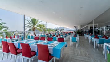Un'ampia zona pranzo all'aperto con tavoli e sedie, ampie finestre e vista mare.