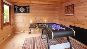 A wooden room with a foosball table, dartboards, and a framed artwork. - Meadowcroft (Watchet)