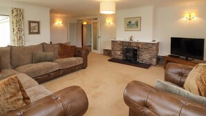 A living room with a fireplace, a sofa set, a television, and wall-mounted lights. - Meadowcroft (Watchet)
