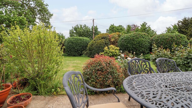A patio with a round table and chairs, surrounded by various plants and a well-maintained lawn. - Meadowcroft (Watchet)