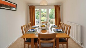 A dining room with a table set for four, chairs, a radiator, and a window with curtains. - Meadowcroft (Watchet)