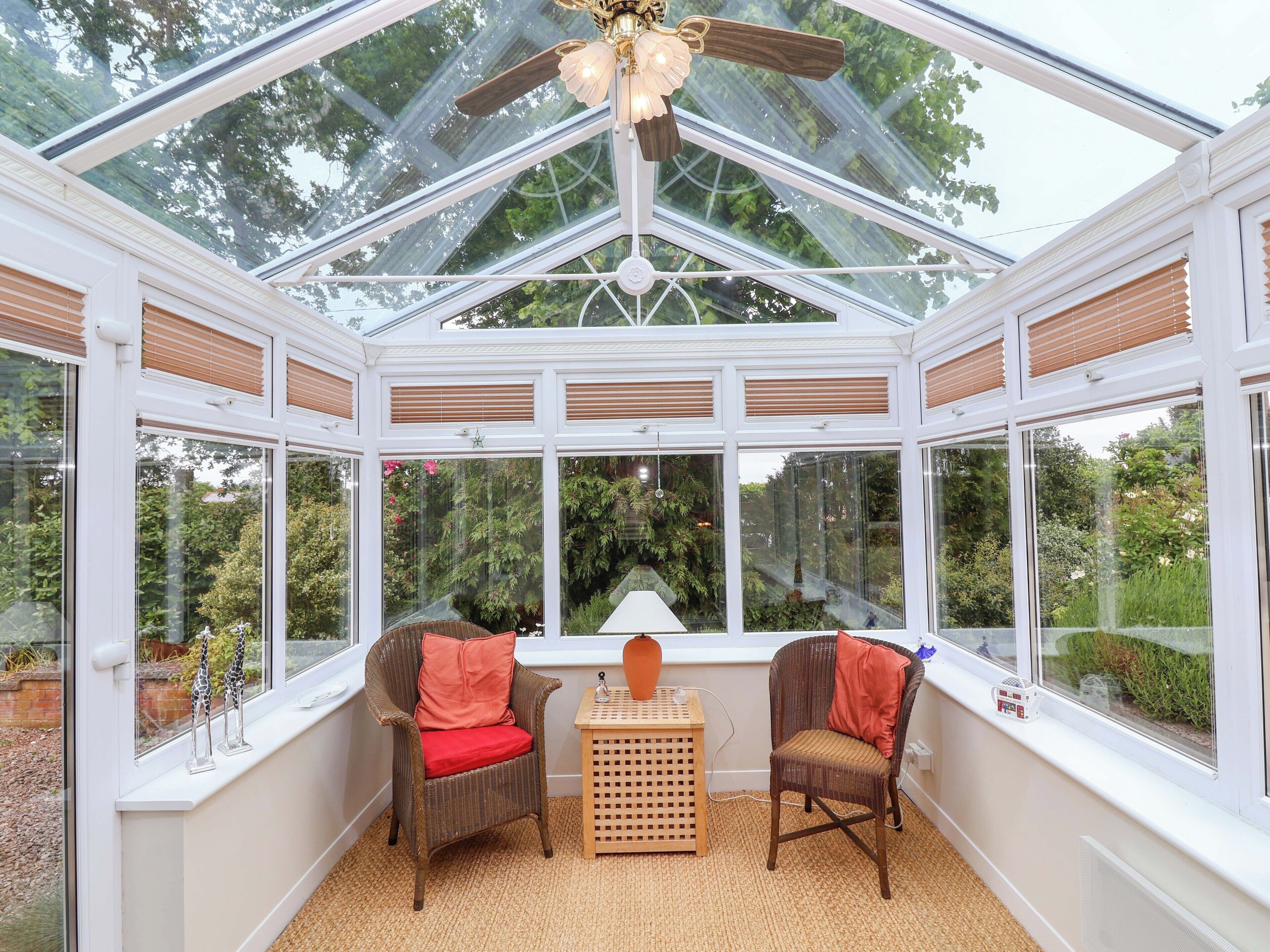 A conservatory with a glass ceiling, wicker furniture, and a small table.