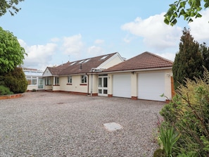 Ein zweigeschossiges Haus mit Schotterauffahrt, einer Garage und einem Wintergarten.