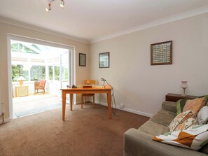A living room with a sofa, a table, and a chair. There is a window with a view of greenery outside. - Meadowcroft (Watchet)
