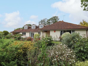 A two-story house with a tiled roof, surrounded by a garden with various plants and flowers. - Meadowcroft (Watchet)