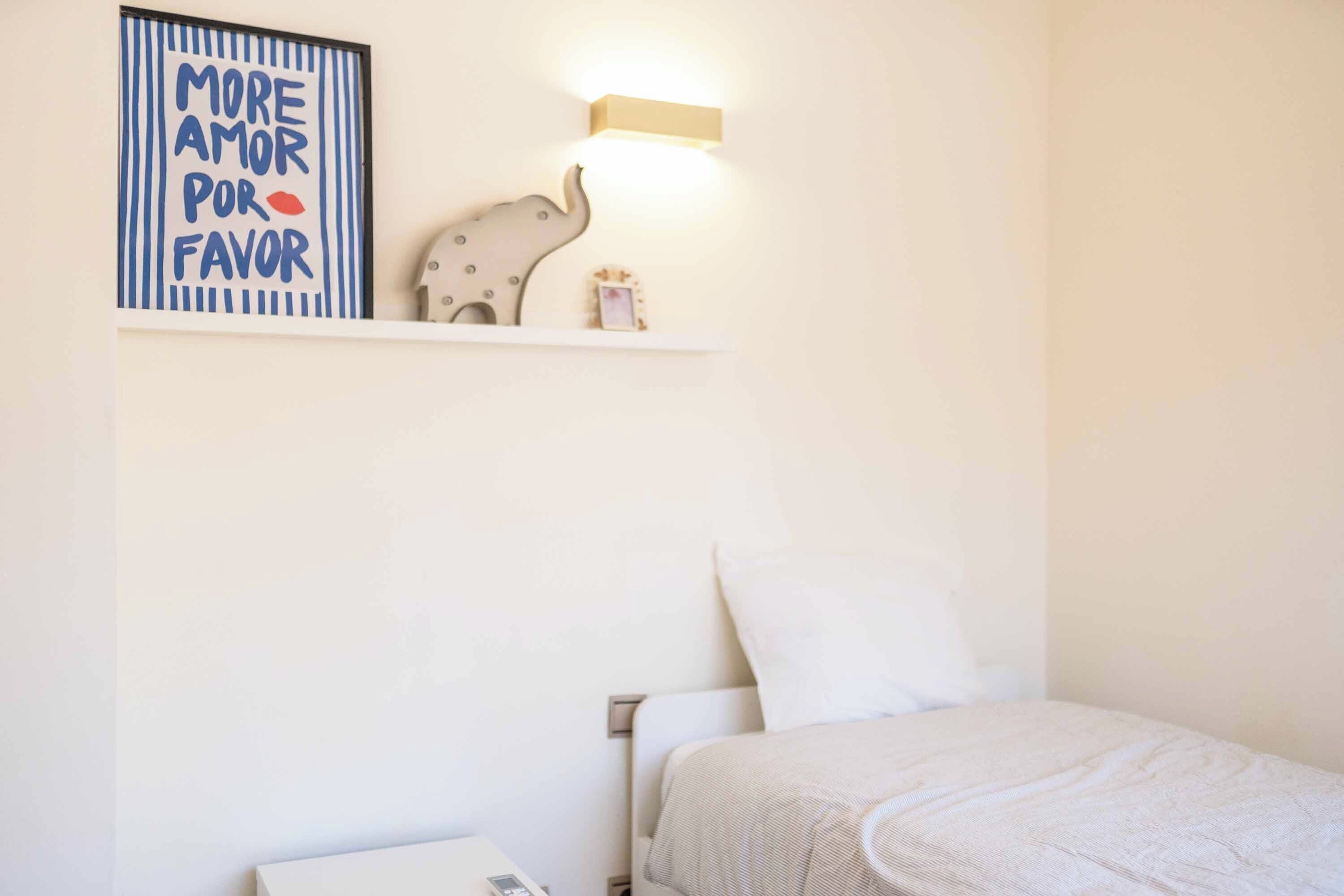 Een slaapkamer met een bed, nachtkastje, een wandplank met decoratieve objecten en een kunstwerk aan de muur.