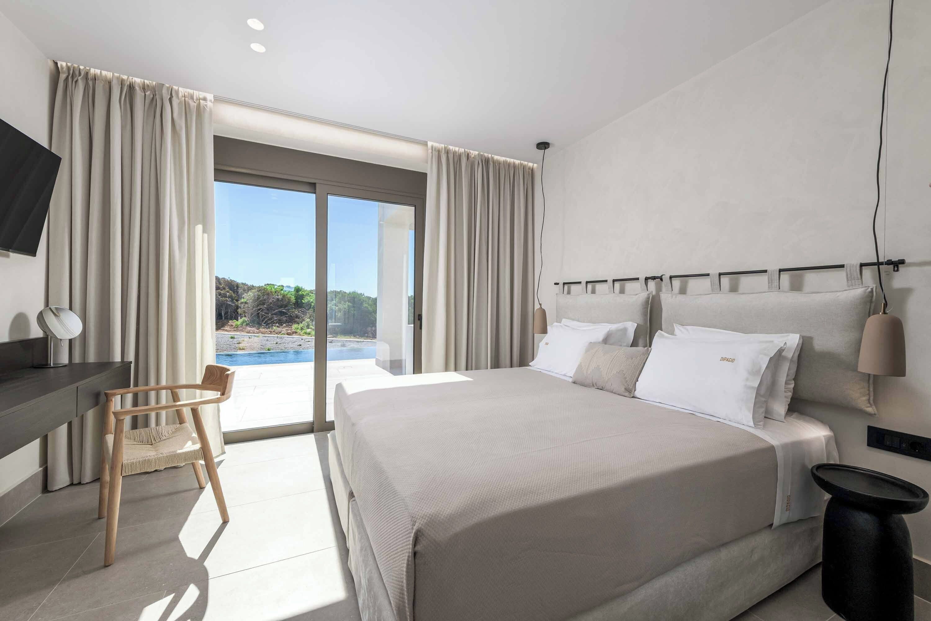 A modern hotel room with a large bed, a desk, a chair, and a view of the outdoors.