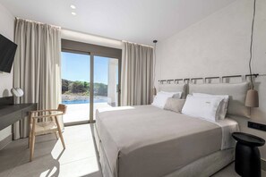 Ein modernes Hotelzimmer mit einem großen Bett, einem Schreibtisch, einem Sessel und Blick ins Freie.