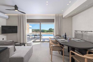 Ein modernes Hotelzimmer mit Essbereich, Flachbildfernseher, Deckenventilator und Blick ins Freie.