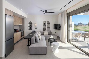 Eine moderne Küche mit integriertem Kühlschrank, einem Essbereich mit großem Tisch und Sitzgelegenheiten sowie einem Wohnbereich mit Sofa und Fernseher.