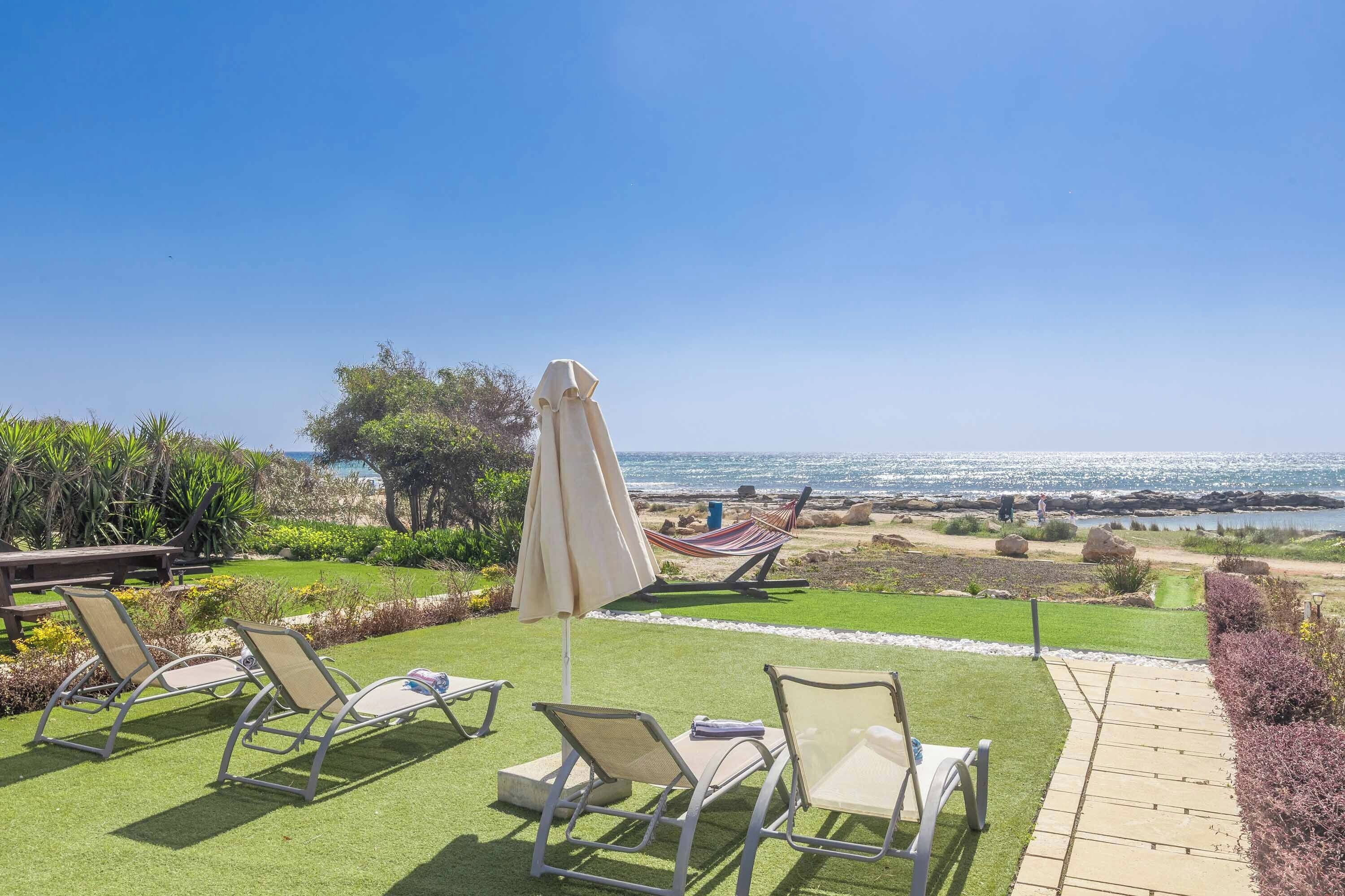 A patio with lawn chairs and an umbrella, a hammock, and a view of the ocean.