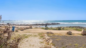 Ein Strand mit felsigem Gelände, wolkenlosem Himmel und dem Meer im Hintergrund.