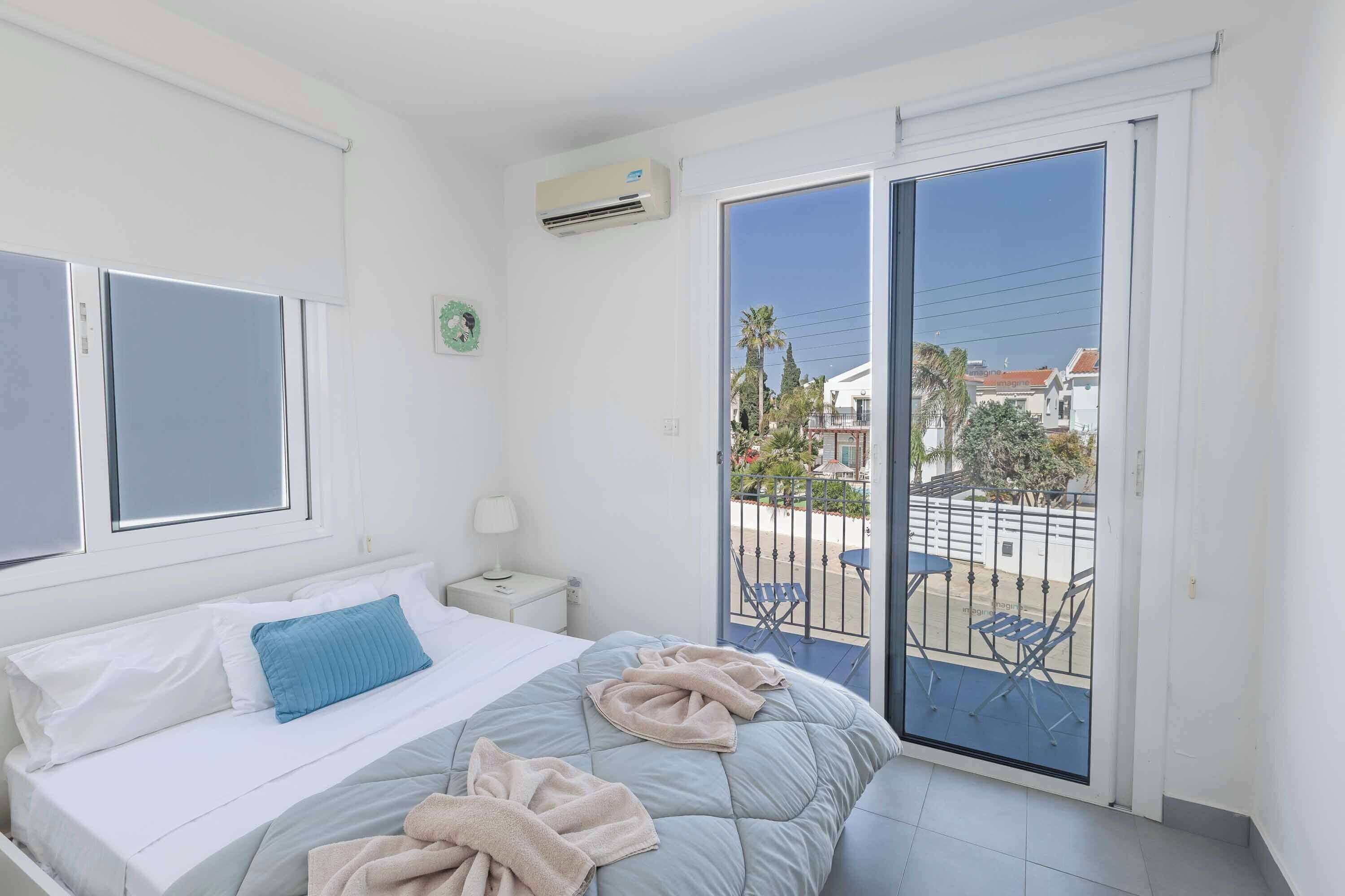 Een slaapkamer met een bed, nachtkastje, raam en balkon met stoelen.