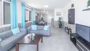 Ein Wohnzimmer mit einer Couch, einem Couchtisch, einem Fernseher und einem Essbereich im Hintergrund.