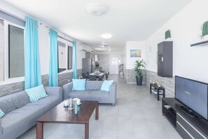 Ein Wohnzimmer mit einer Couch, einem Couchtisch, einem Fernseher und einem Essbereich im Hintergrund.
