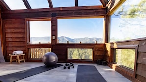Eine Holzhütte mit großen Fenstern, Trainingsgeräten und Blick auf die Berge.