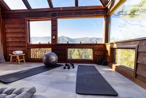 Eine Holzhütte mit großen Fenstern, Trainingsgeräten und Blick auf die Berge.