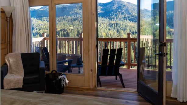 Ein Zimmer mit Holzboden, großen Fenstern, einem Balkon mit Stühlen und Bergblick.