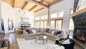 Ein geräumiges Wohnzimmer mit einem Ecksofa, einem Kamin und großen Fenstern.