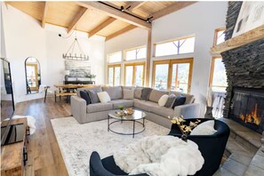 Ein geräumiges Wohnzimmer mit einem Ecksofa, einem Kamin und großen Fenstern.