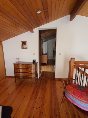 A room with wooden flooring, a dresser, a chair, and a doorway leading to another room.