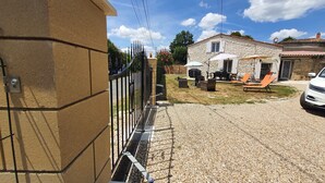 A stone house with a gravel driveway, outdoor seating, and a white car parked nearby.