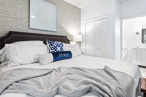 Ein ordentlich bezogenes Bett mit einem Kissen mit der Aufschrift '101 BLUE', einer Nachttischlampe und einem gerahmten Kunstwerk an der Wand.