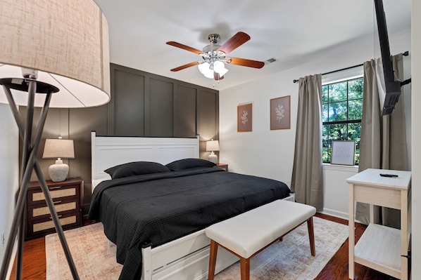 A bedroom with a bed, bedside tables, a ceiling fan, a window with curtains, and a TV.