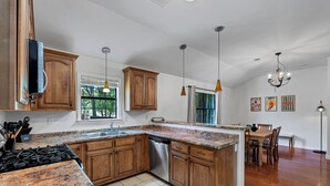 A kitchen with wooden cabinets, granite countertops, a dishwasher, and a dining area with a table and chairs. - Game Room+Xbox, 15 Min to Memphis & Tunica Casino (Horn Lake)