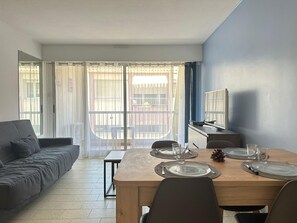 Ein Essbereich mit einem Tisch für vier Personen, einer Couch, einem Fernseher und einem Balkon mit Blick.