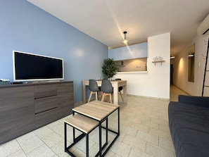 Ein modernes Wohnzimmer mit Flachbildfernseher, einem kleinen Holztisch, einer Couch und einer Küchenzeile mit Esstisch und Stühlen.