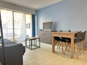 Ein modernes Wohnzimmer mit Essbereich, Fernseher und einem Balkon mit Vorhängen.