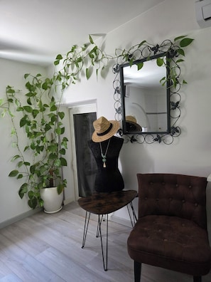 Ein Zimmer mit Blumentopf, einer Büste mit Hut, einem Spiegel und einem braunen Stuhl.