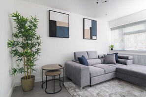 Een moderne woonkamer met een grijze modulaire bank, een klein rond tafeltje, een grote pot met bamboe en abstracte wanddecoratie.