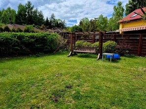 A wooden swing set, a bench, and a small table in a grassy backyard with a wooden fence and trees in the background.
