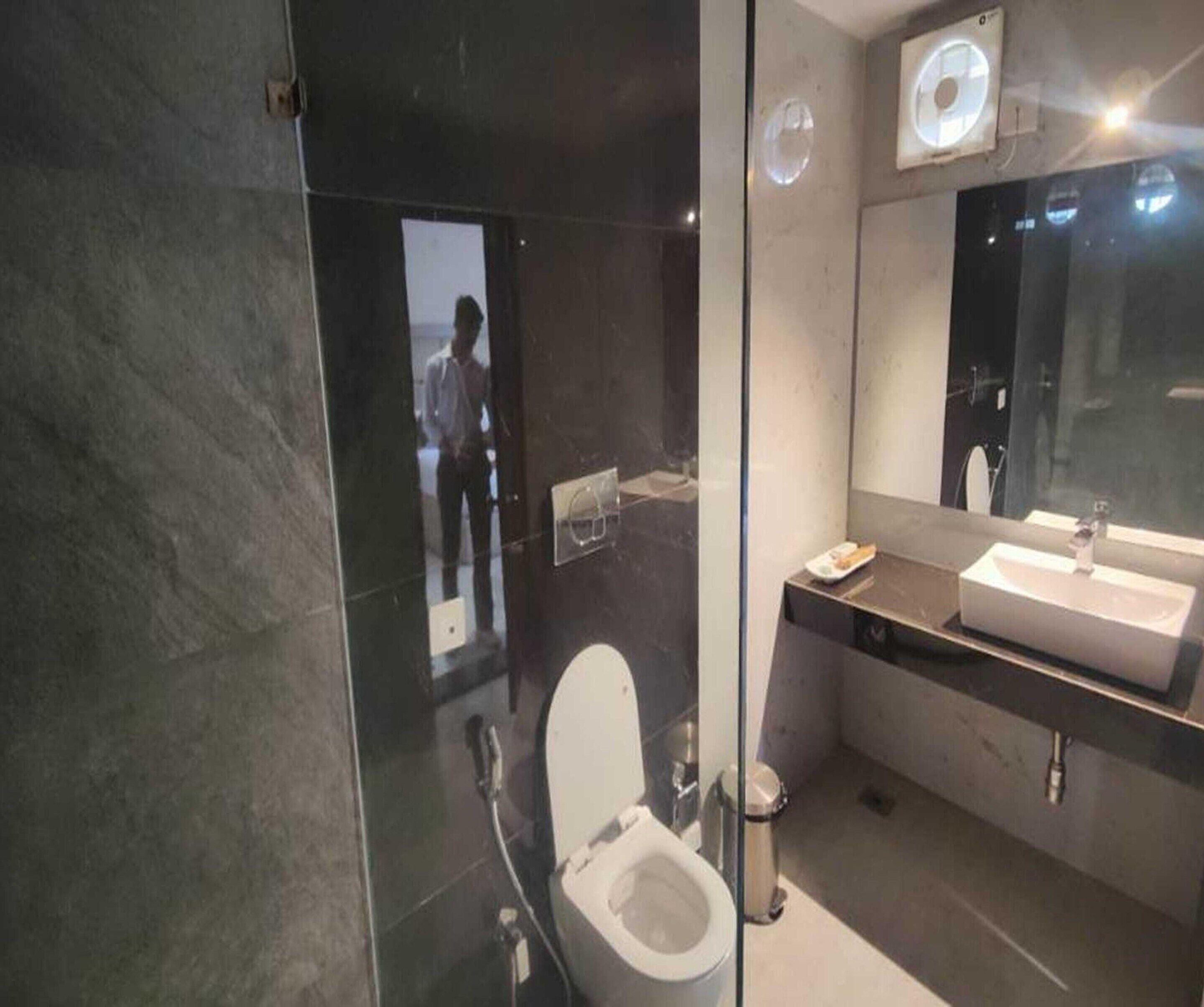 A modern bathroom with a glass partition, a toilet, a sink, and a mirror.