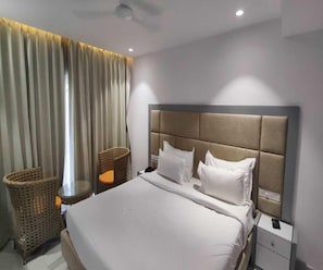 A hotel room with a bed, a nightstand, a lamp, a wicker chair, and a window with curtains.