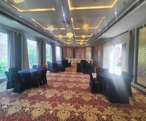 Une salle de conférence dotée d’un tapis à motifs, de tables rondes et de chaises, de grandes fenêtres et de lustres.