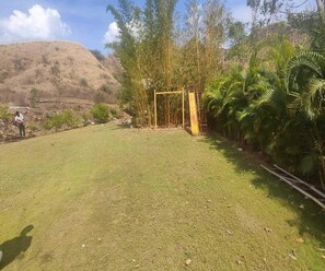 A grassy area with a yellow gate, surrounded by trees and a hill in the background. - 1bhk Nature View Villa With Private Balcony (Udaipur)