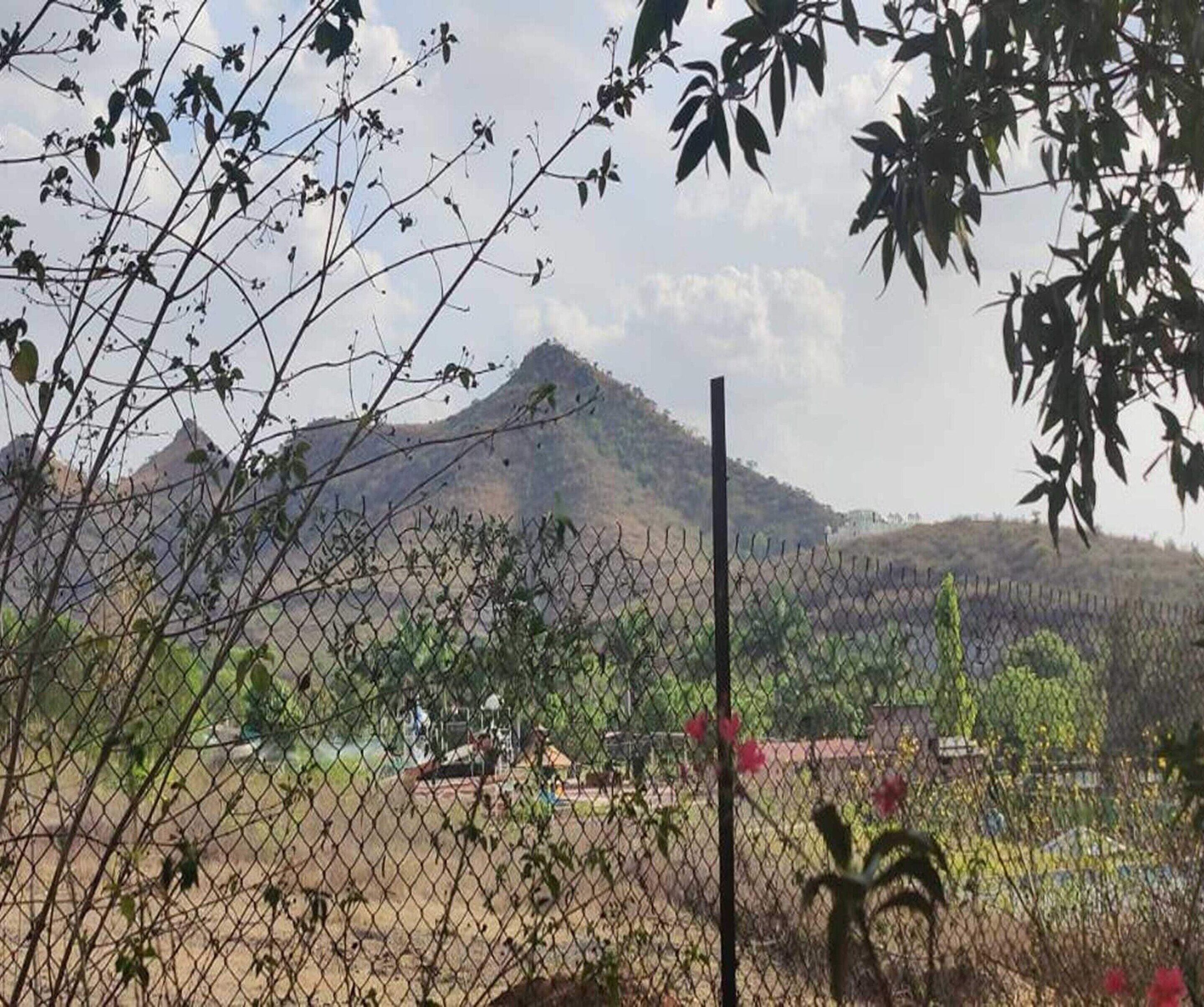 Un área cercada con una montaña al fondo, cielo despejado y algo de vegetación.