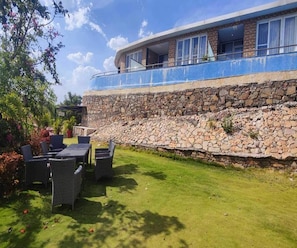 A stone retaining wall, outdoor seating, and a building with large windows. - 1bhk Nature View Villa With Private Balcony (Udaipur)